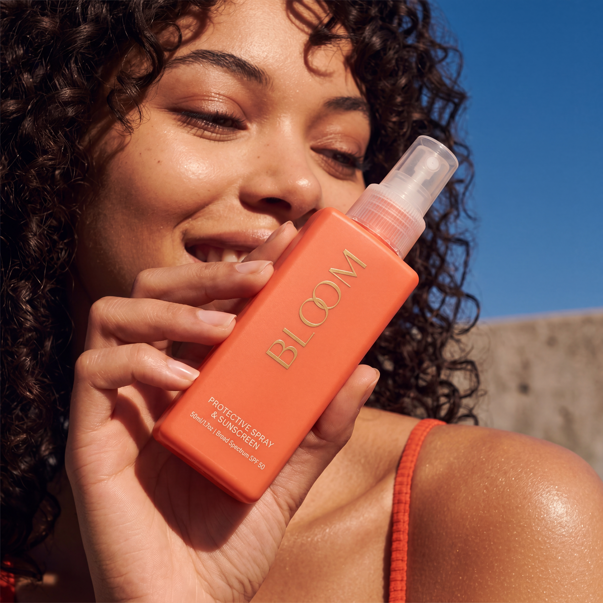 Close-up beauty campaign image featuring an orange Bloom sunscreen bottle.